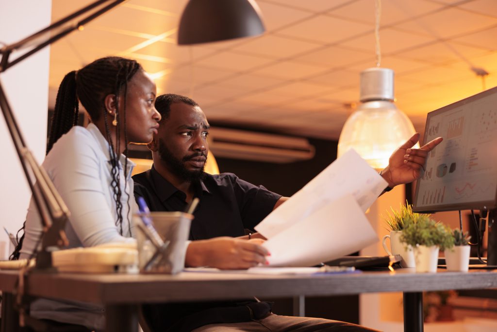 african american man woman doing teamwork collaboration presentation report looking data computer papers working together with paperwork office sunset